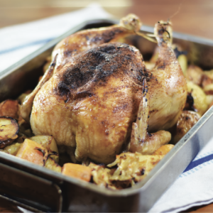 Roast chicken on roasting tray surrounded by potatoes