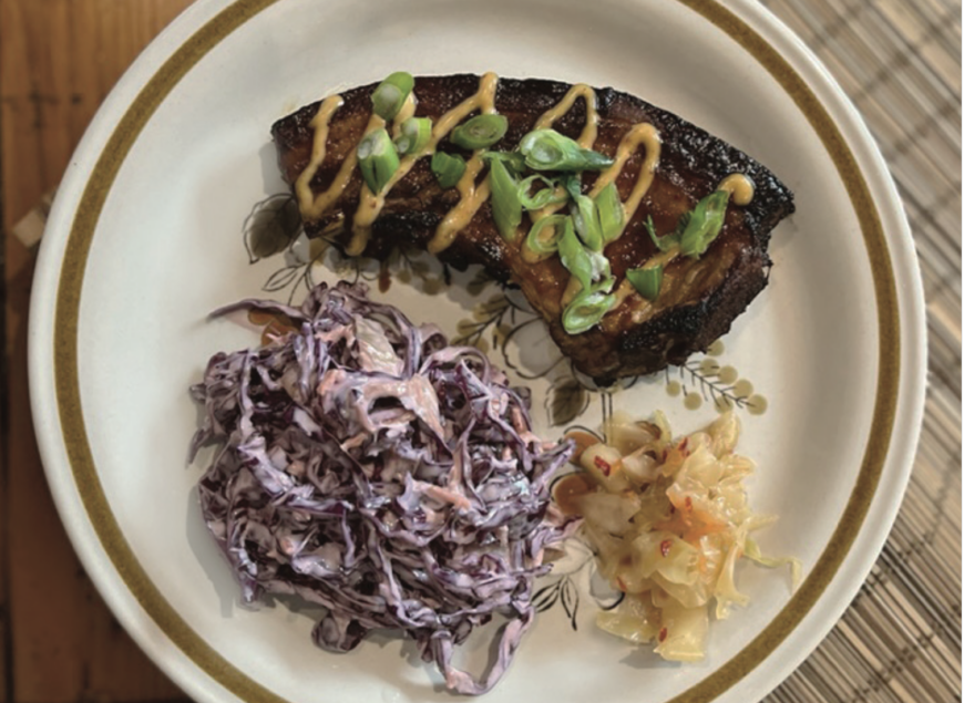 A pork chop on a plate with coleslaw and kimchi